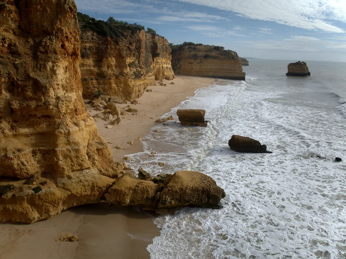 Waves along the long shore at Praia da Marinha with sea stacks in the distance