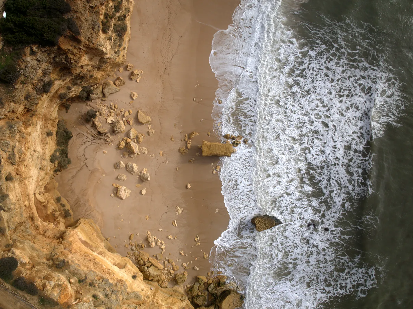 Fallen rocks on the sand at the foot of the cliff at Praia da Marinha, seen from directly above