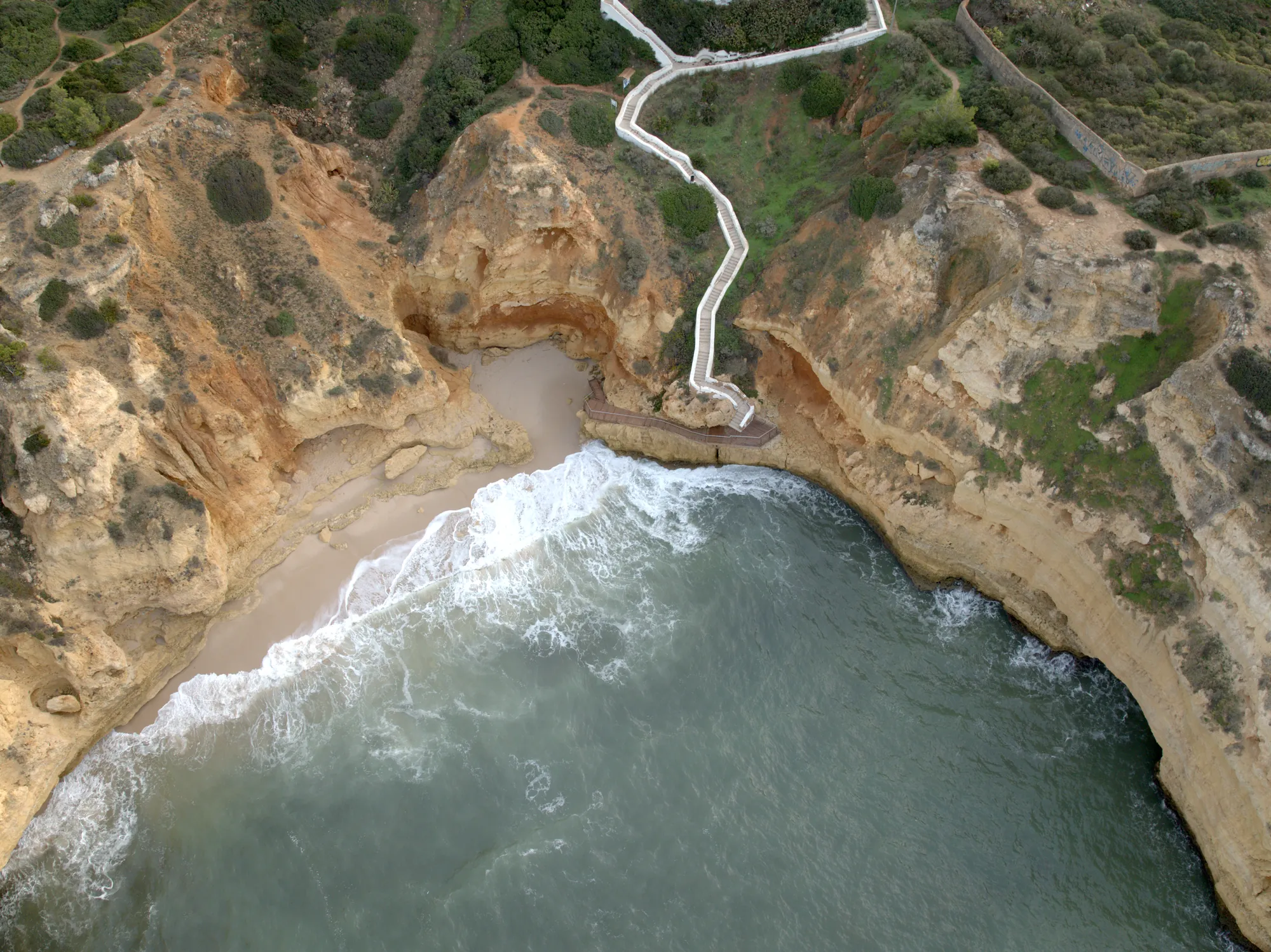 Praia do Paraíso from the air: a small sandy cove under cliffs with a zigzag staircase coming down