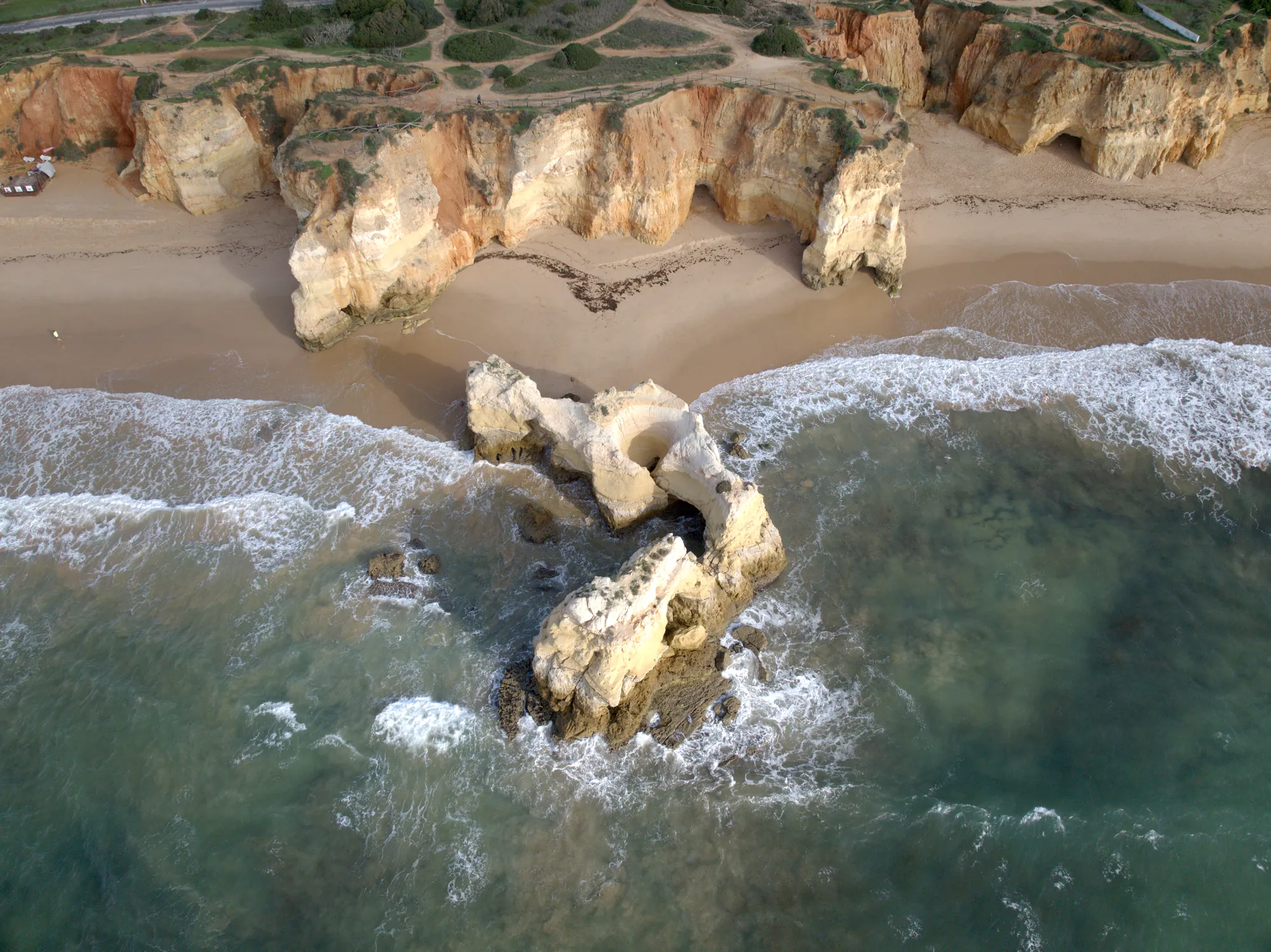 Praia do Vau from the air, with ochre cliffs and a large rock standing in the surf
