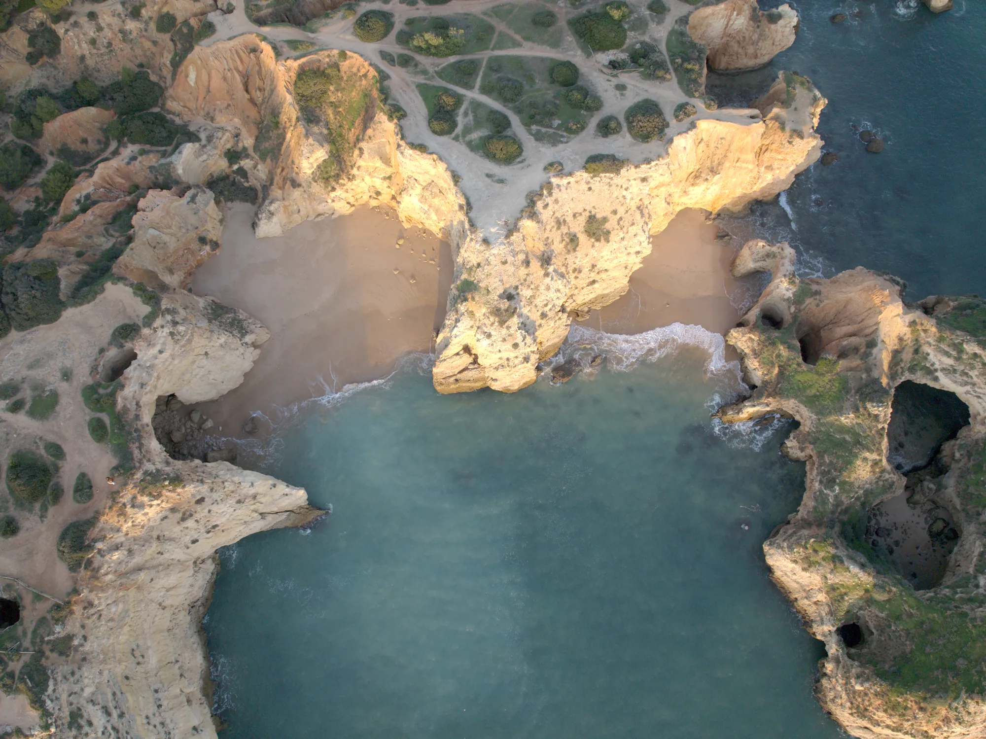 The coves of Praia João de Arens from the air, split by a rocky point and surrounded by cliffs